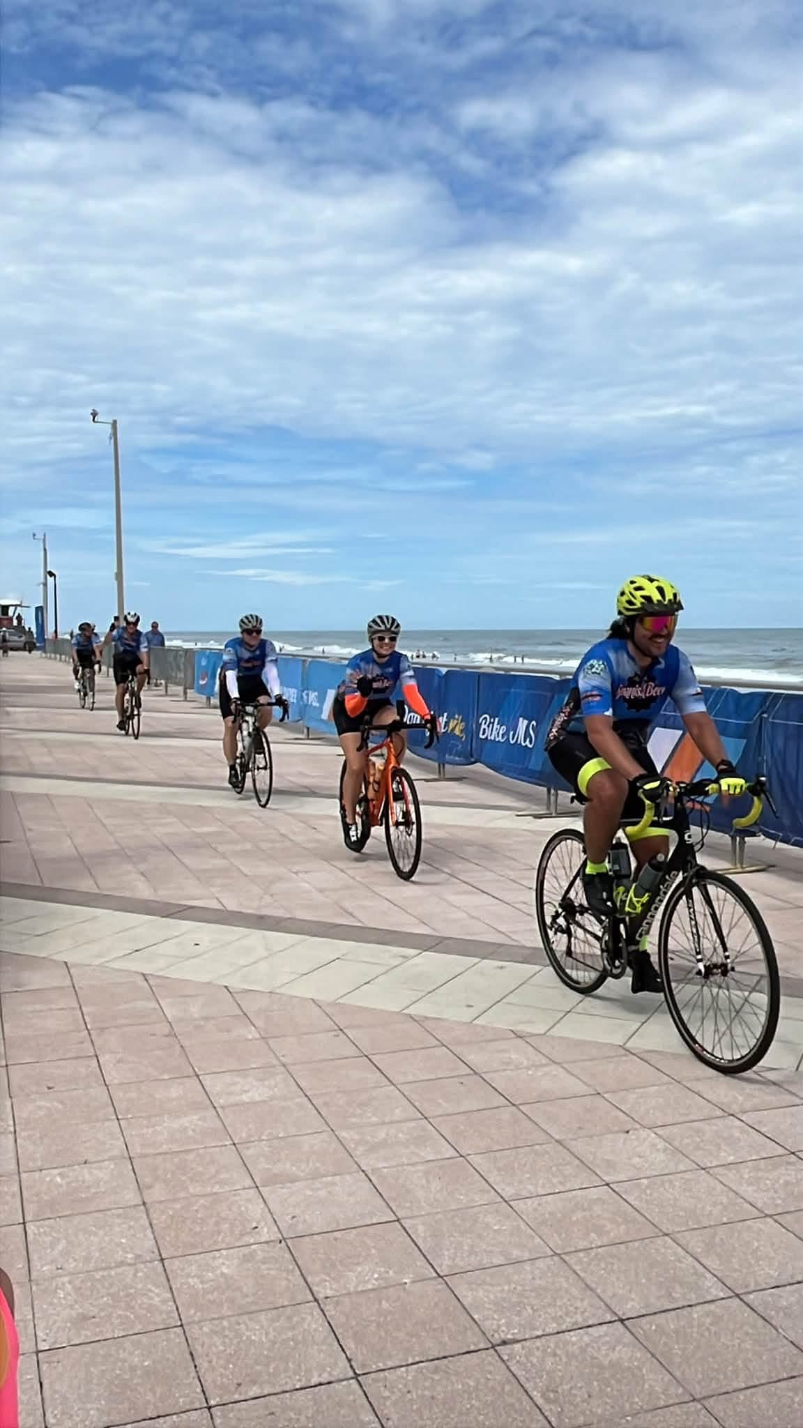 Andrew in a yellow helmet leads Selena, who waves from her orange bike, along the beach boardwalk