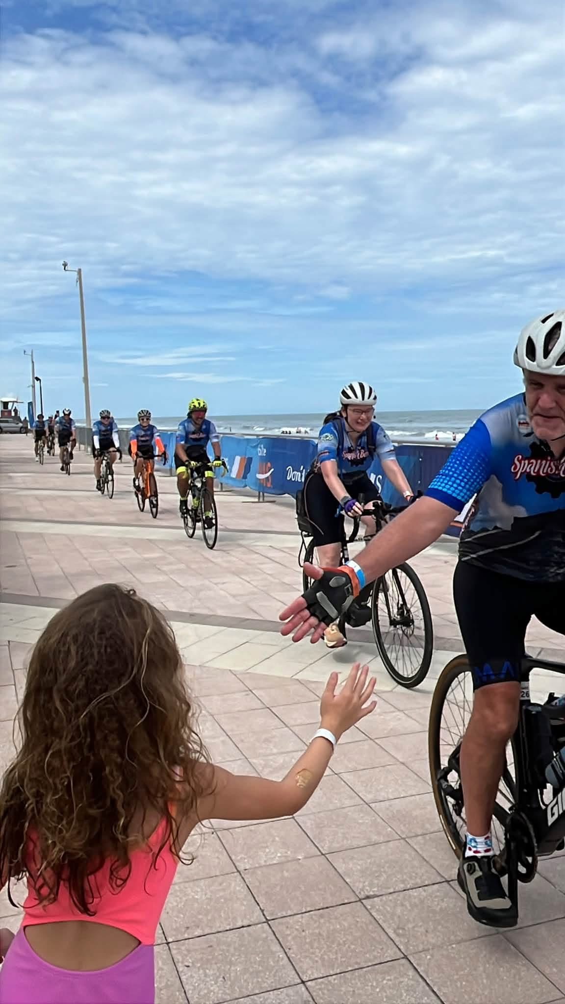 A young girl high-fives a Team Spanish Beer rider as the team rides along the beach boardwalk to the finish