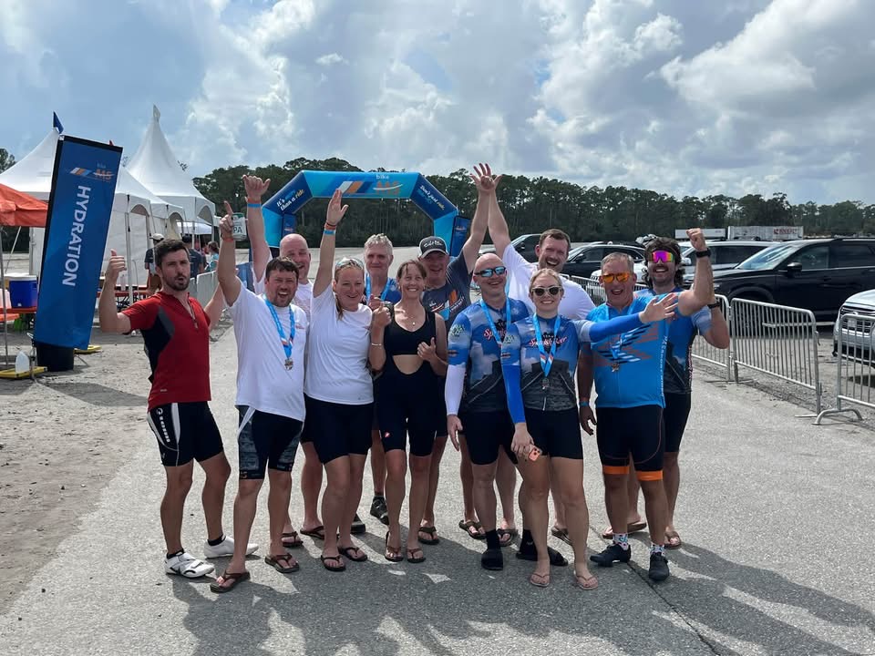 Team Spanish Beer riders wearing finisher medals and cheering in front of the Bike MS finish arch